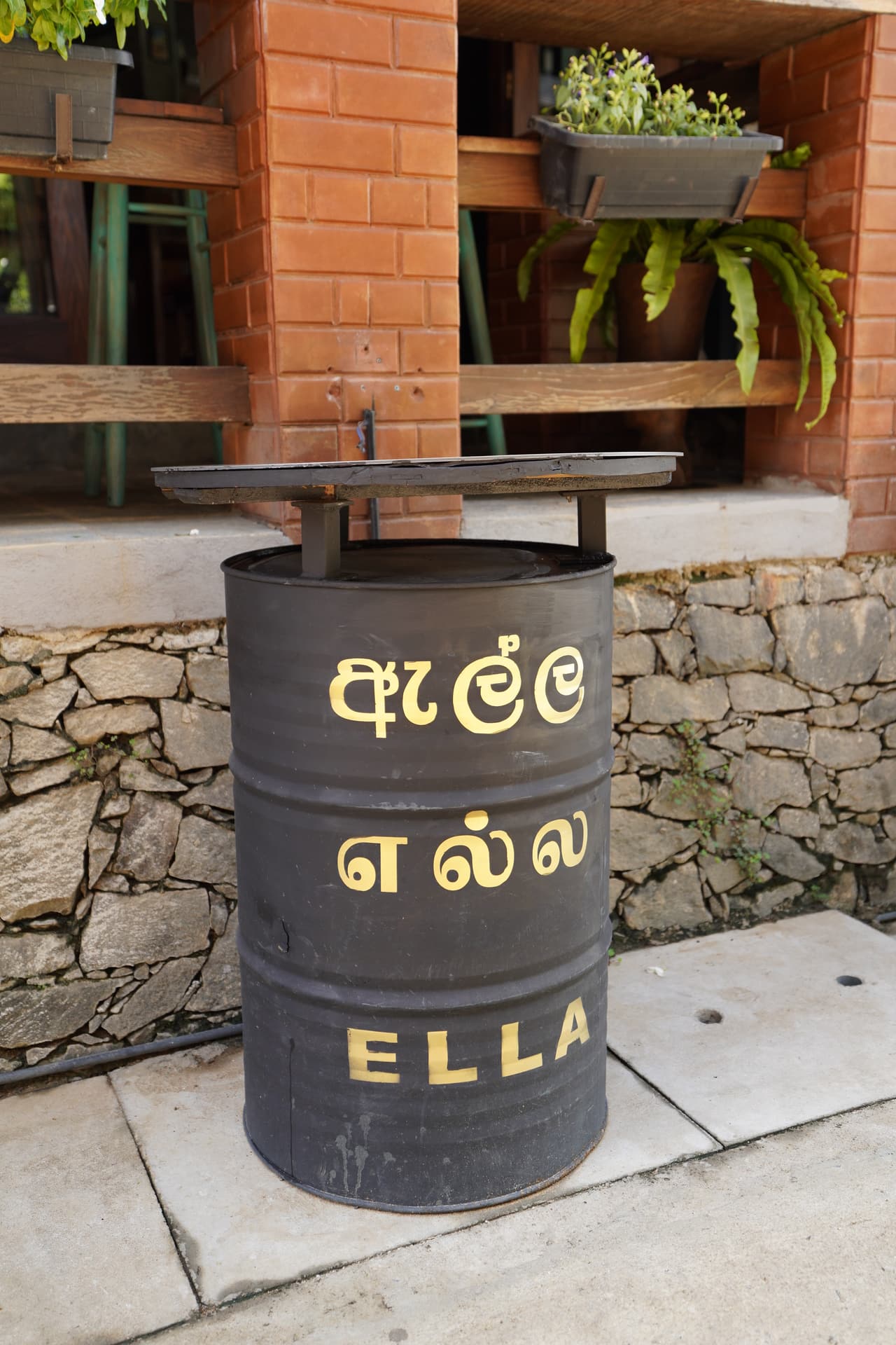 A painted oil drum at the entrance to AK Ristoro, Ella — “Ella” written in Sinhala, Tamil and English