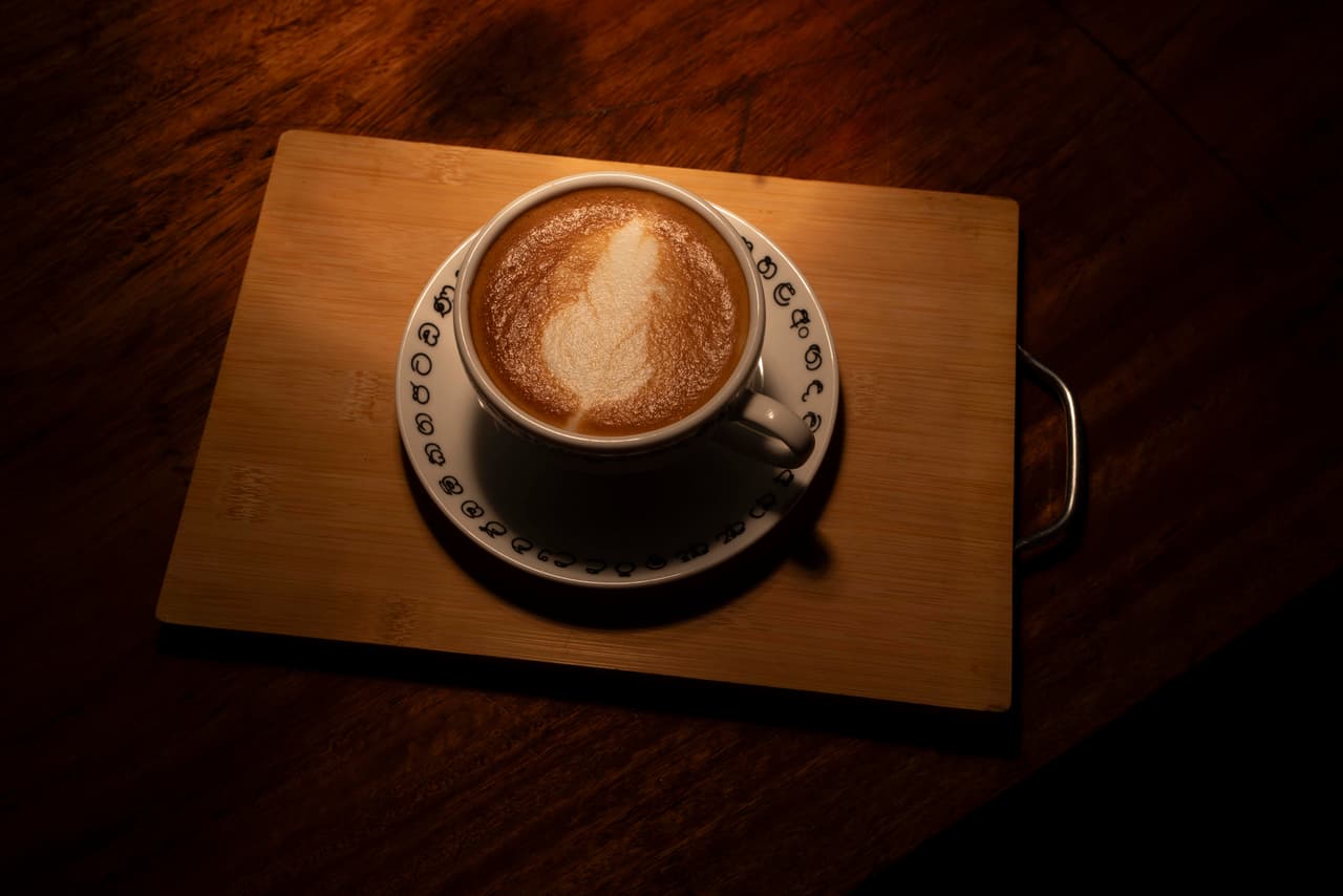 A cappuccino with latte art at AK Ristoro, Ella — a patterned cup and saucer on a wooden board