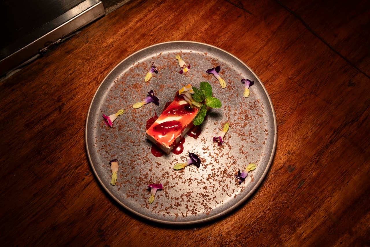 Cheesecake at AK Ristoro, Ella — a berry glaze, mint and scattered edible flowers on a grey plate