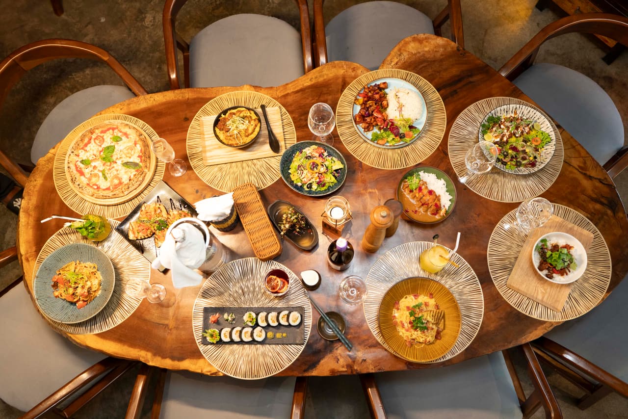A feast on a live-edge table at AK Ristoro, Ella, seen from above — pizza, sushi, katsu curry, pasta and salads for eight