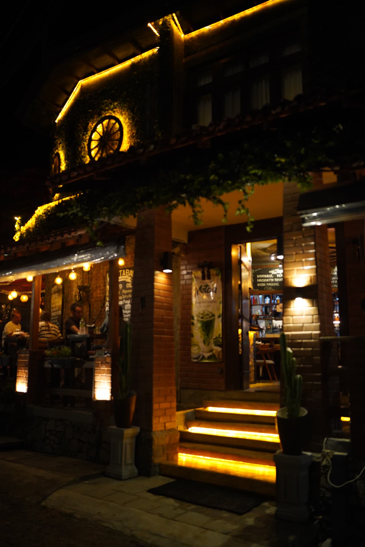 The entrance to AK Ristoro, Ella, at night — lit timber steps up to the dining room under a wagon wheel