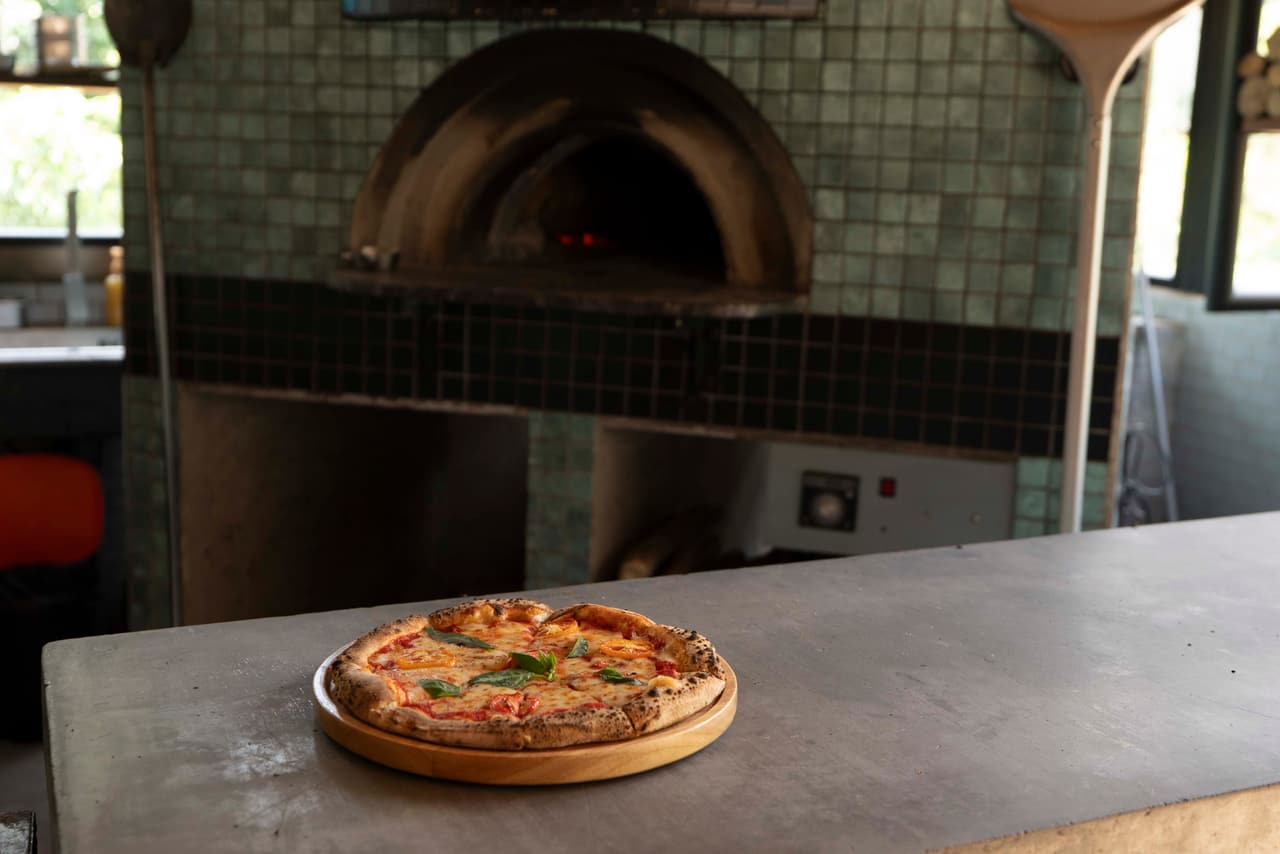 A Margherita on a wooden board in front of the tiled wood-fired oven at AK Ristoro, Ella