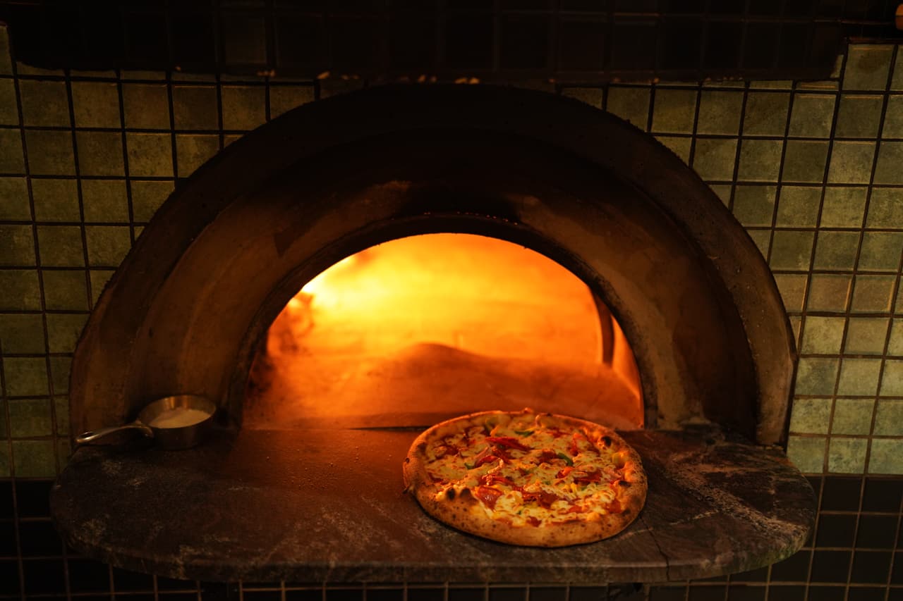 A pizza at the edge of the glowing wood-fired oven at AK Ristoro, Ella — green tiles around the arch