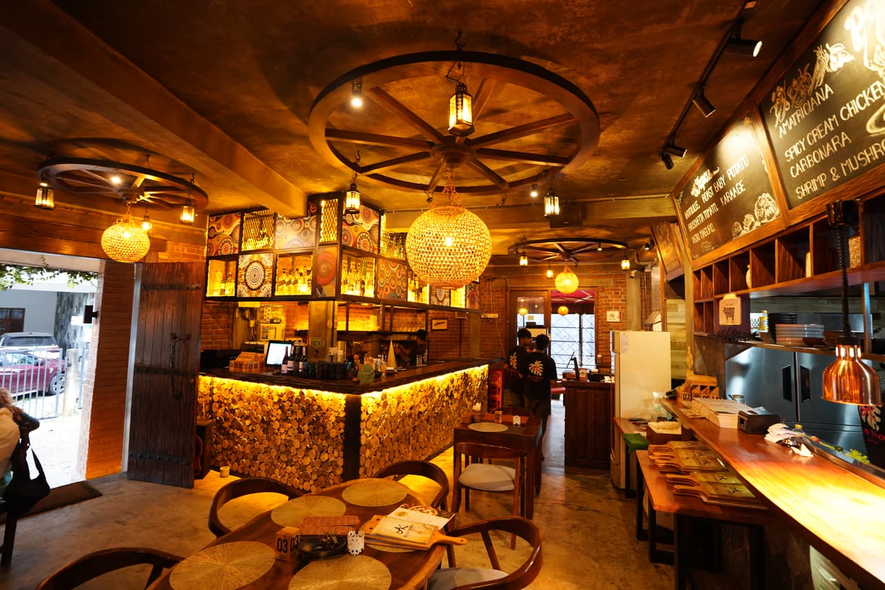 La sala del bar di AK Ristoro, Ella — lampadari a ruota di carro, lampade intrecciate e lavagne con il menu sopra il bancone