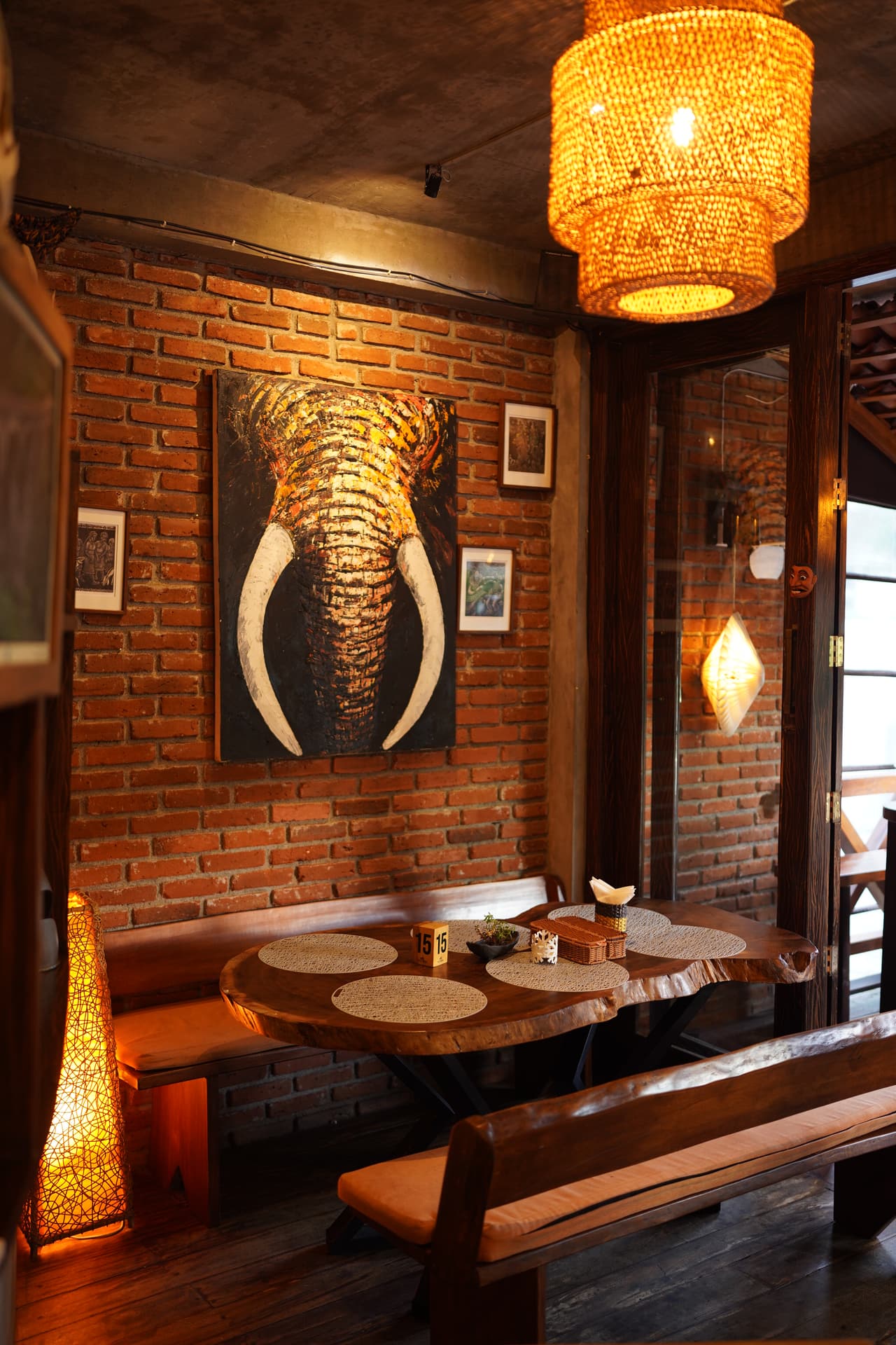 A brick-walled booth at AK Ristoro, Ella — an elephant painting and a woven lantern above a table for six