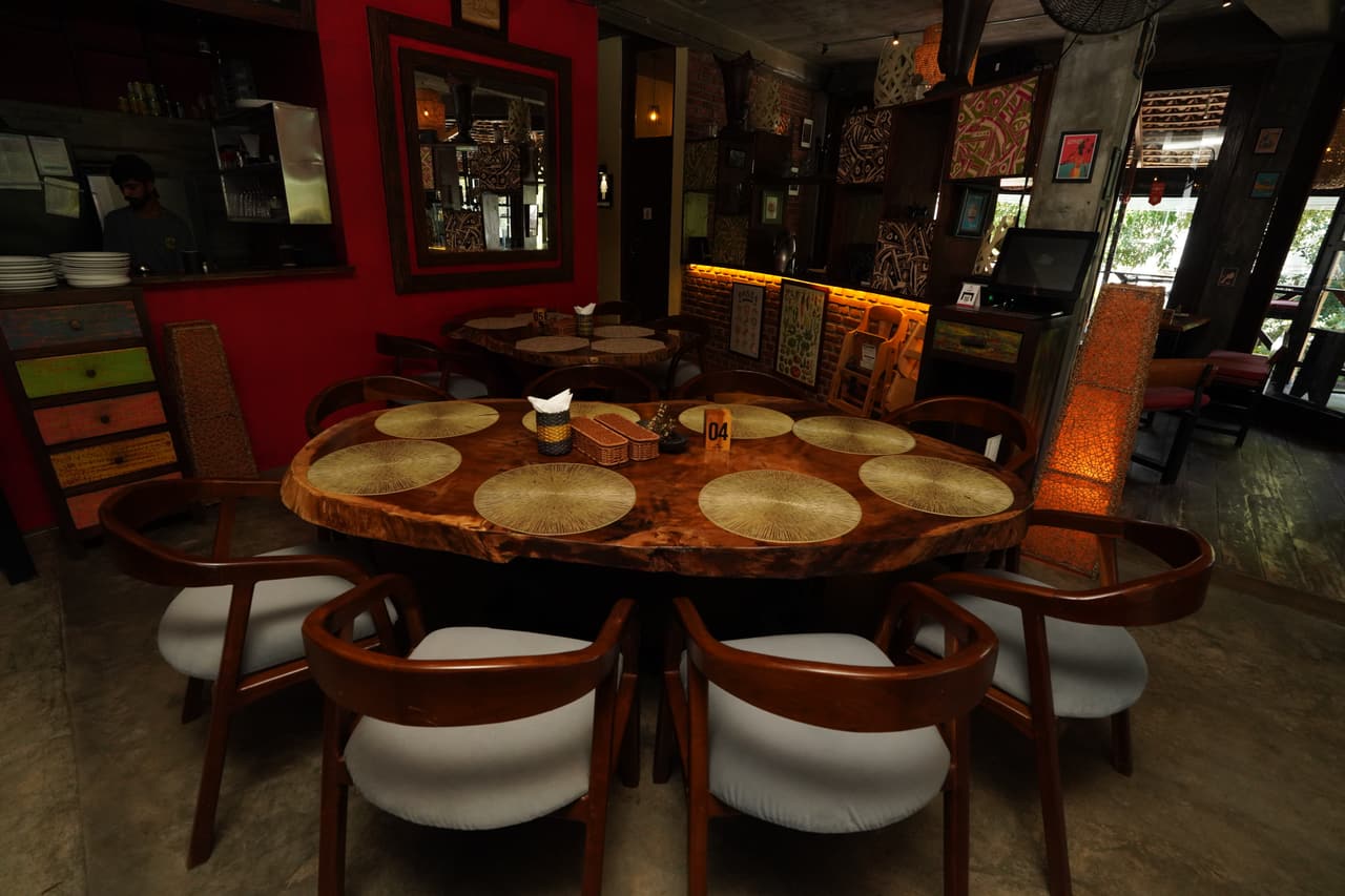 A table laid for eight at AK Ristoro, Ella — a live-edge table and grey chairs against a red wall