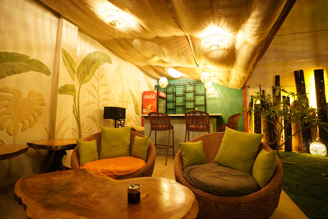 The garden pavilion at AK Ristoro, Ella — round wicker chairs with green cushions, a live-edge table and banana-leaf murals